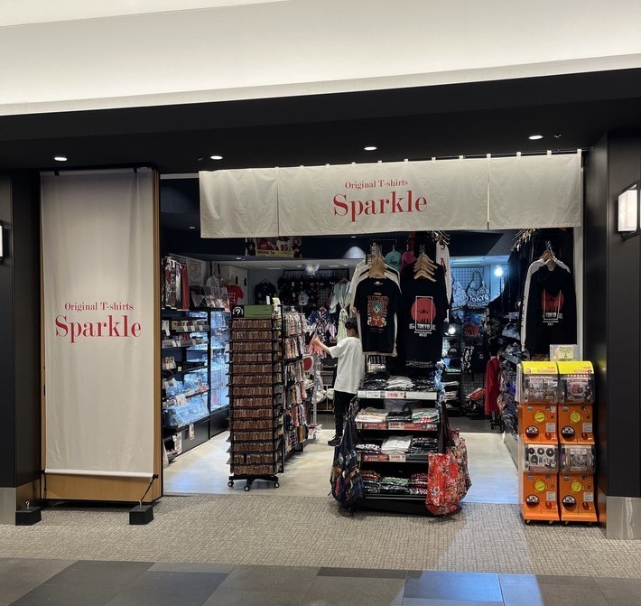 羽田エアポートガーデンSPARKLEの店舗入口。暖簾とTシャツ・雑貨の売場